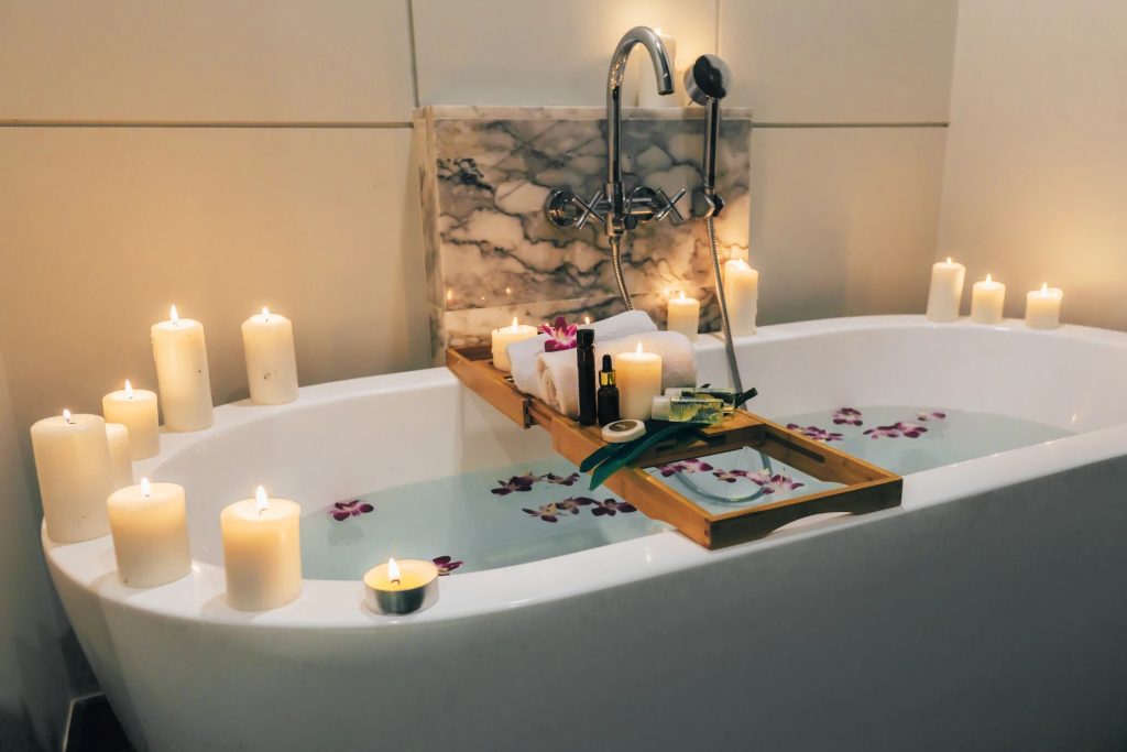 Freestanding bathtub filled with water and petals, surrounded by candles and bath accessories in a calm bathroom